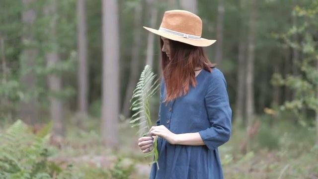Young woman in brown hat and blue dress shirt with long hair walking in the pine tree forest