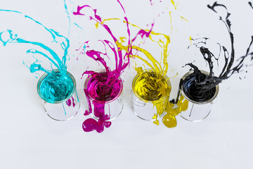 Fontänen aus den Druckfarben CMYK spritzen aus vier Eimern in den Raum
