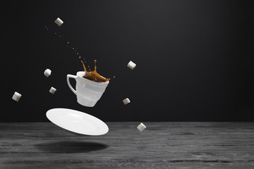 Floating cup of coffee, saucer and lump sugar over a black wooden table. Splashes of black coffee in a white cup.