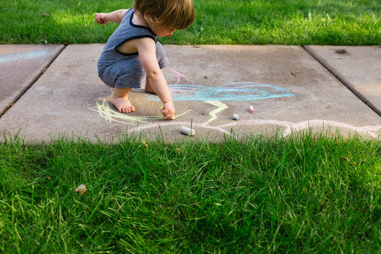 A young boy draws with chalks outside in the summer.