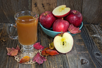 apple cider in glass mug with apples and autumn leaves on rustic wood