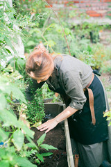 Young cute lady working at the garden with wildflowers wearing linen dress, black apron and leather belt with florist tools