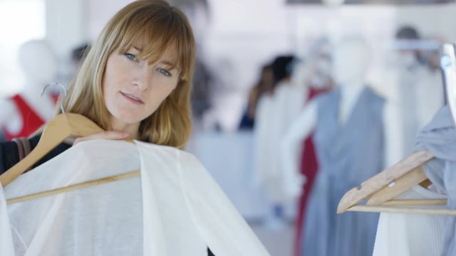 Customer holding up garment and looking into mirror in fashion clothing store. Seen from mirror's pov with other customer's shopping in background.