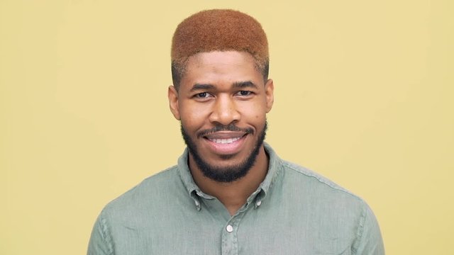 slow motion picture of metis man with dyed hair in red looking at camera looking at camera smiling nodding positively over yellow background closeup. Concept of emotions