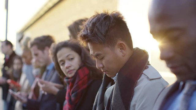  Diverse business group looking at smartphones while waiting in line