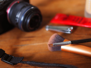 Obraz na płótnie Canvas Short makeup brush, blurred nail clippers, cream cosmetic, beauty tools, black camera with straps on red brown wooden texture table top background, perspective, to prepare as a photo-shooting model