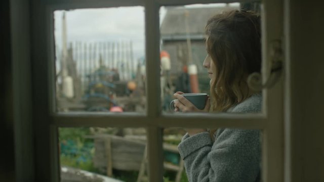  Young woman at beach house drinking coffee & looking out at the view