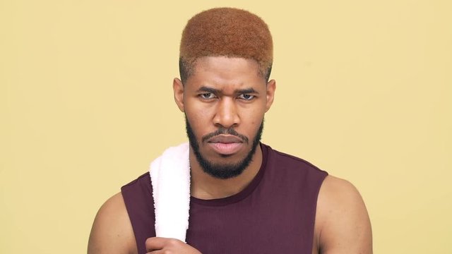 slow motion sporty strong metis guy with stylish haircut wearing workout clothes taking break after training putting white towel on shoulder isolated over yellow background closeup