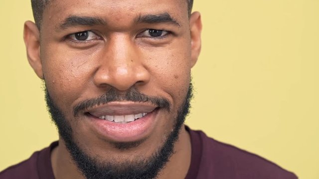 picture of dark-skinned bearded guy expressing happiness smiling nodding positively over yellow background extreme closeup in slow motion. Concept of emotions