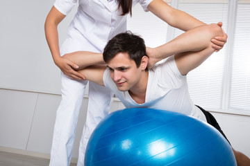 Physiotherapist Assisting Man While Doing Exercise