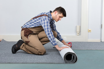 Male Handyman Rolling Carpet On Floor