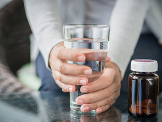 Closeup young woman holding drinking water glass in her hand with pills bottle. Health care concept.