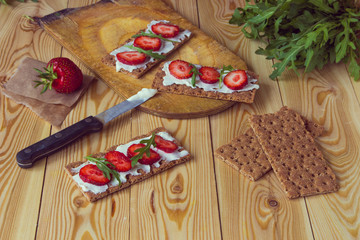 Wholegrain rye crispbread crackers with cream cheese, strawberry and arugula