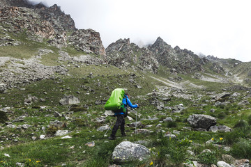 Tourist with large backpack hiking in the mountains, around high rocks and beautiful nature. Mountain tops in snow