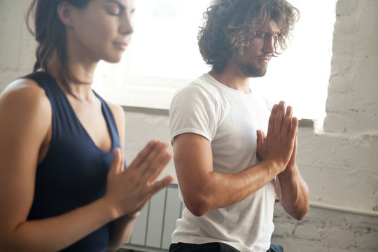 Group of young sporty people making namaste gesture, man and woman meditating, practicing yoga lesson with instructor, working out, indoor close up image, studio. Wellbeing and wellness concept