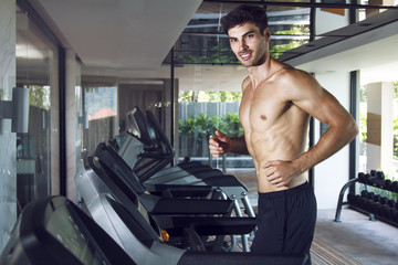 Naklejka premium Young healthy handsome man training in the gym on the treadmill. Running with smile and without t-shirt. 