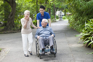 An old couple walking in the park with help from care workers