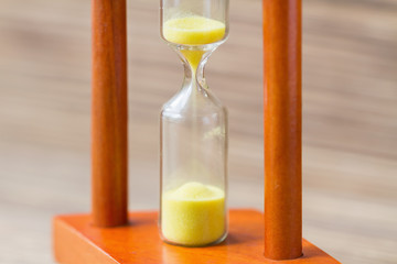 Time passing concept. Hourglass with yellow sand on wooden background. Closeup, selective focus