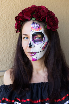 Sugar Skull Halloween Makeup.  Dia de los Muertos. Brunette girl with Mexican style Halloween face painting. Red rose, flower hair decor