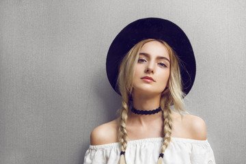 Close up of beautiful young blonde woman with black hat. Her hair is tied in two big ponytails....