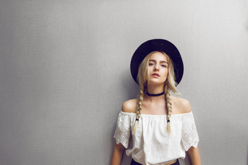 Close up of beautiful young blonde woman with black hat. Her hair is tied in two big ponytails. Around neck she has black choker.