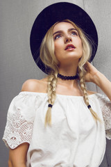 Close up of beautiful young blonde woman with black hat. Her hair is tied in two big ponytails. Around neck she has black choker.