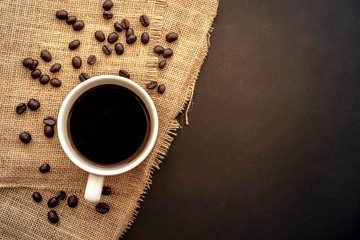 A cup of coffee and coffee bean grain on sack fabric put on black wood table background include copyspace for add text or graphic