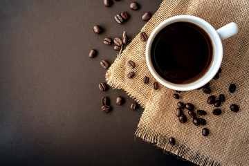 A cup of coffee and coffee bean grain on sack fabric put on black wood table background include copyspace for add text or graphic