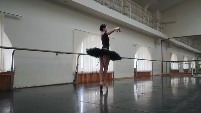Ballerina in black tutu dancing classical pas in ballet gym. Woman alone practicing before performance. Slow motion. Young beautiful lady working out with amazing dance.