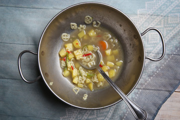 Macaroni soup with vegetables. Pasta soup in metal bowl top view.
