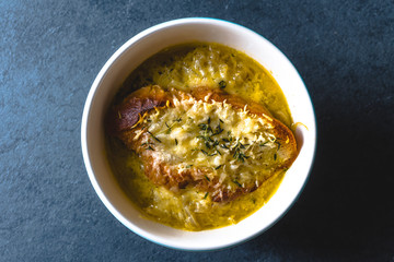 Onion soup with cheese, croutons and thyme in a ceramic bowl on a blue stone