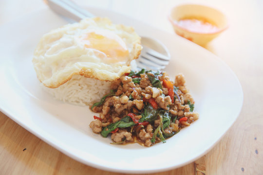 stir fried pork and basil with rice and egg on wood background thai food