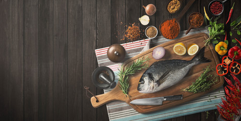 Fresh fish on wooden tables arranged with spices and vegetables. Top view