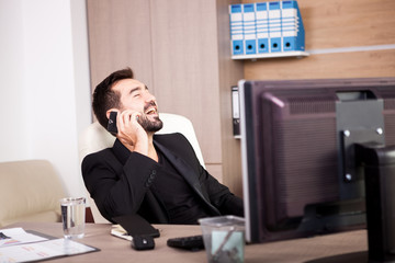 Laughing Businessman talking on the phone while working in his office. Businessperson in professional environment