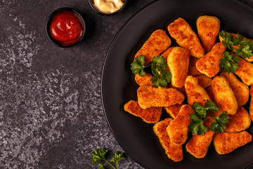 Chicken nuggets with sauces on dark background.