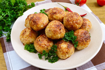 A pile of golden meat balls on a plate with parsley on a wooden table.