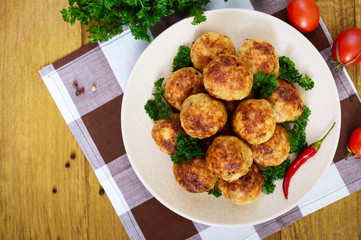A pile of golden meat balls on a plate with parsley on a wooden table. Top view.