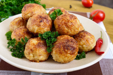 A pile of golden meat balls on a plate with parsley on a wooden table. Close-up