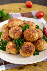 A pile of golden meat balls on a plate with parsley on a wooden table. Close-up. Vertical view
