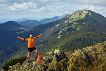 Hiker with backpack standing on top of a mountain with raised hands