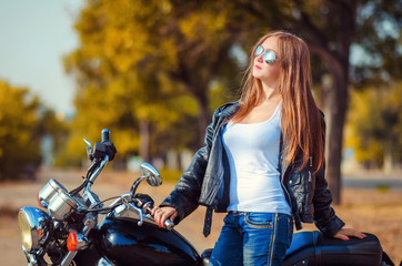 Fototapeta na wymiar young woman in a leather jacket and blue jeans in a glasses stand with a motorbike