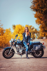 Fototapeta na wymiar beautiful girl in a leather jacket and blue jeans in a glasses on a motorbike