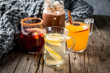 Selection of various autumn traditional drinks: hot chocolate with marshmallow, tea with lemon and ginger, white pumpkin spicy sangria, mulled wine. On wooden rustic table, copy space, selective focus