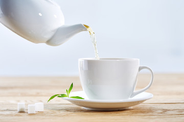 Pouring green tea from white ceramic teapot