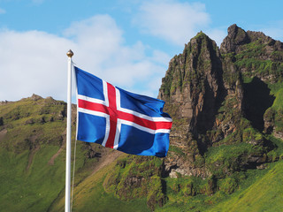 Flag of Iceland against the background of green mountains and blue sky