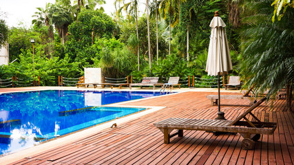 Wooden sunbed with umbrella on modern swimming pool
