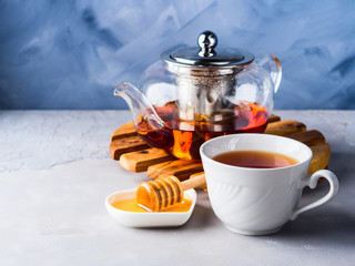 Cup of red tea rooibos and honey with glass teapot on blue