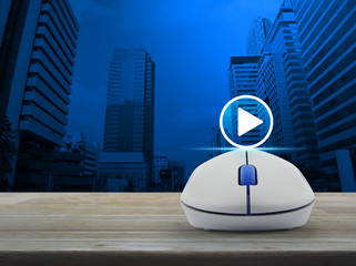 Play button with wireless computer mouse on wooden table over modern office city tower, Business music online concept