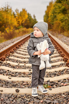 lost a lonely little boy in old-fashioned gray clothes hugs a bunny in the middle of the forest on abandoned railway rails
