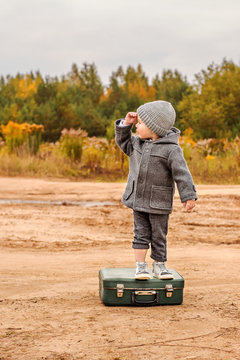 little boy in retro gray clothes climbed on an old suitcase in search of